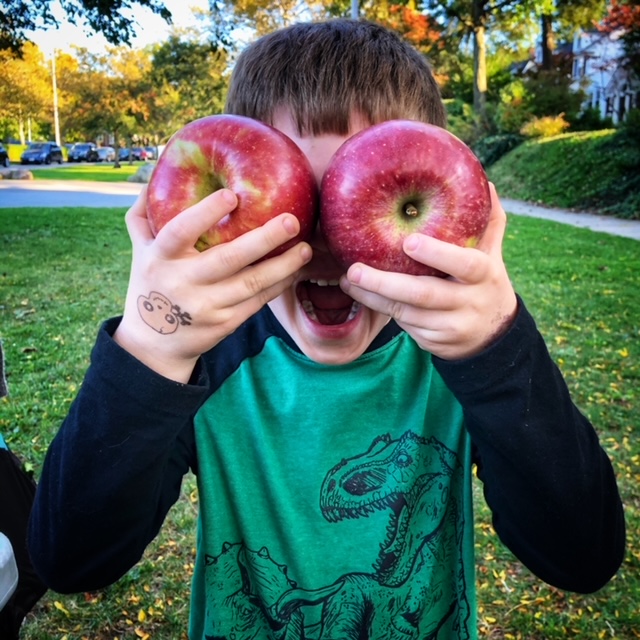 Boy with huge crisp apples held in front of his face like big googly eyes.
